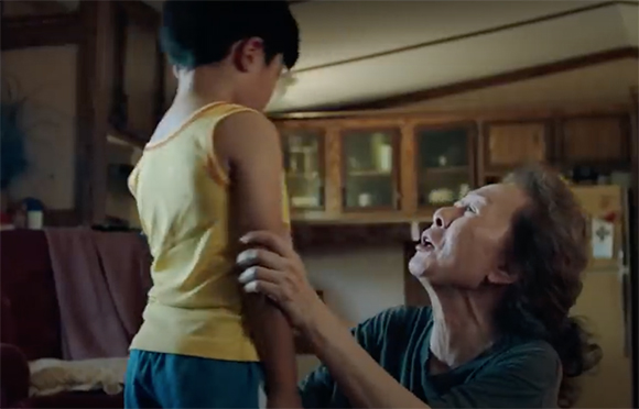 A woman looks up at a young boy standing in front of her in a dimly lit room.