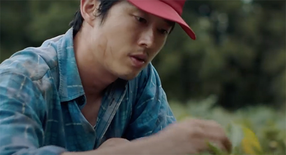 A man wearing a red cap and a blue plaid shirt looks downward toward the ground.