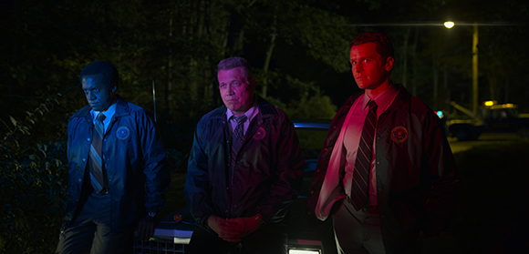 Three men in professional jackets and ties stand together in a dark, outdoor setting under dim lighting.