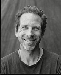 A smiling man with wavy hair and a light beard looking toward the camera.