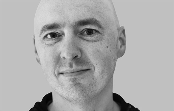 Black and white close-up portrait of a bald man looking directly at the camera.