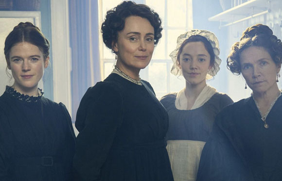 Four women in 19th-century attire standing in a brightly lit room.