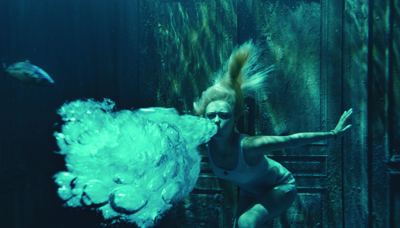 A person underwater blowing a large, bright cloud of bubbles against a dark, textured background.