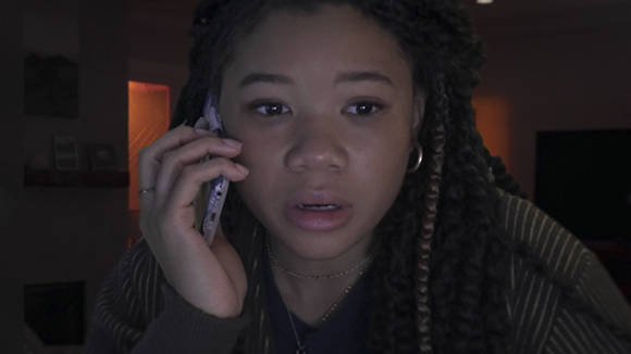 A young woman with long braids holds a phone to her ear with a surprised expression.