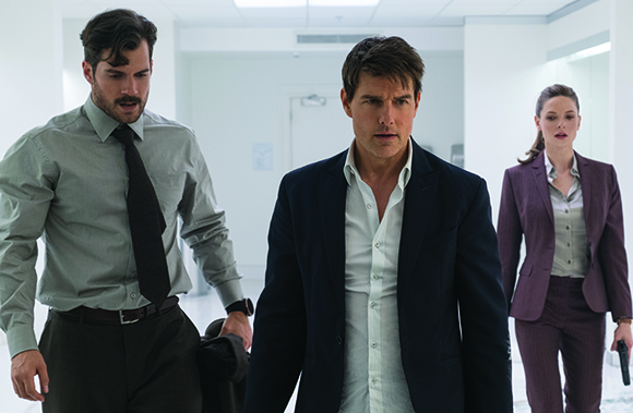 Three people in professional attire walk through a brightly lit, white hallway.