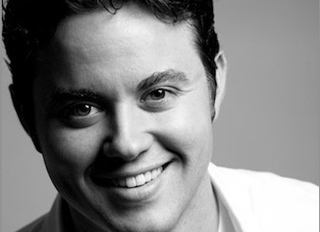 Black and white close-up portrait of a smiling man looking toward the camera.