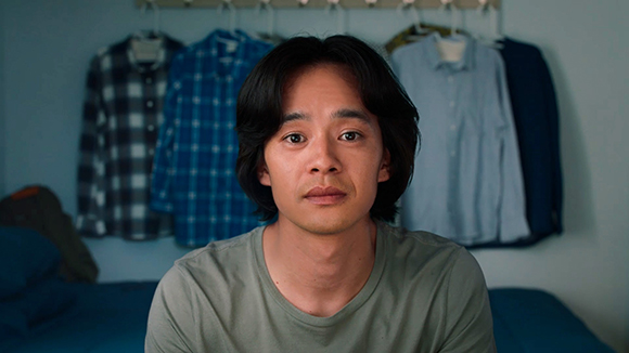 A man with dark hair and a neutral expression wearing a grey t-shirt.