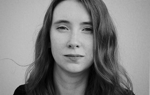 Black and white close-up portrait of a woman with long, wavy hair looking directly at the camera.