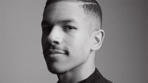 Black and white close-up portrait of a young man looking slightly off-camera against a plain background.
