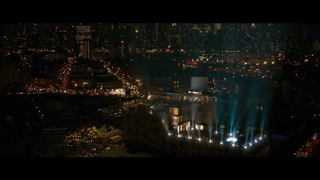 Night view of a city skyline with bright blue and white spotlights shining from a building rooftop.