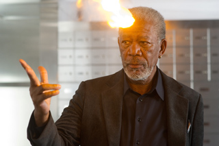 An older man in a dark suit with a flame erupting from his forehead.