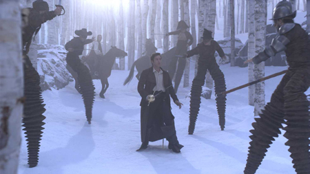 A man with a sword stands in a snowy forest surrounded by figures on tall, jagged stilts.