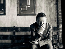 A man in a suit sits on a wooden bench, resting his chin on his hand.