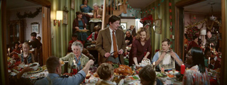 A large multi-generational family sits around a long table filled with food in a decorated dining room.