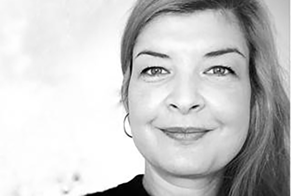 Black and white close-up portrait of a woman with light hair smiling at the camera.