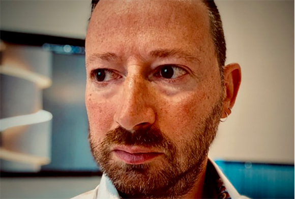 Close-up of a man with short hair, a beard, and a small hoop earring looking off-camera.