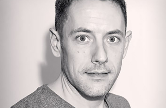 Black and white close-up portrait of a man with short hair looking forward with wide eyes.