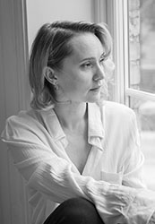 Black and white portrait of a woman with blonde hair looking out a window.
