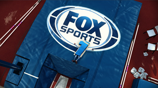 A large Fox Sports logo printed on a blue gymnastics mat in a gym setting.