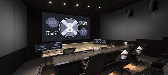 A dark film editing studio featuring a large screen displaying countdown numbers and a long mixing console.