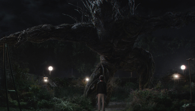 A person stands in front of a giant, dark, gnarled tree with sprawling branches under a night sky.