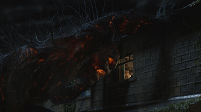 A massive, dark, fibrous creature with glowing orange highlights looms over a stone house at night.
