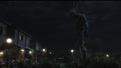 A tall, dark, vine-like creature stands in a garden next to houses under a dark night sky.
