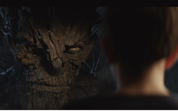 A close-up of a large, textured wooden creature with glowing eyes looking at the back of a person's head.