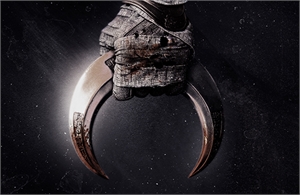 A gloved hand grips a large, curved, metallic crescent blade against a dark, speckled background.