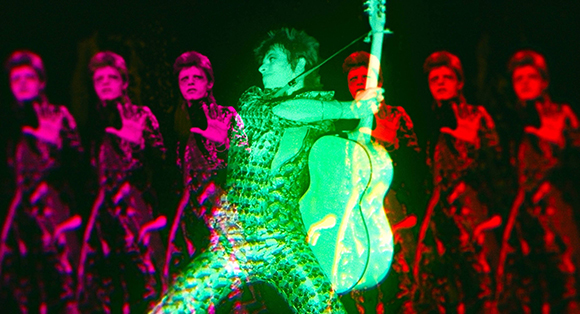 A musician in a patterned outfit plays a guitar amidst several colorful, overlapping silhouettes.