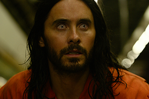 A man with long dark hair, a beard, and pale eyes stares intensely toward the camera.