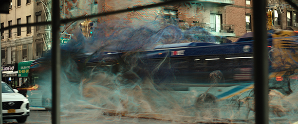 A blue bus moving through thick, swirling white and blue smoke on a city street.