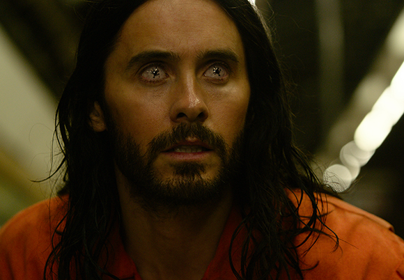 A man with long dark hair, a beard, and pale, clouded eyes wearing an orange garment.