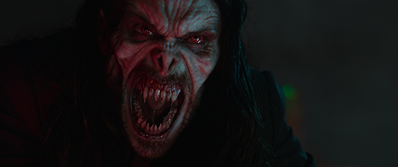 A close-up of a pale, monstrous face with glowing red eyes and a mouth full of sharp, jagged teeth.