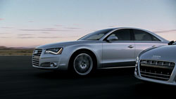 Two silver Audi sedans parked on a dark asphalt surface under a twilight sky.
