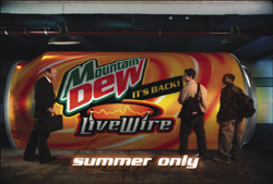 A giant Mountain Dew LiveWire can in a dark space with three people walking past it.