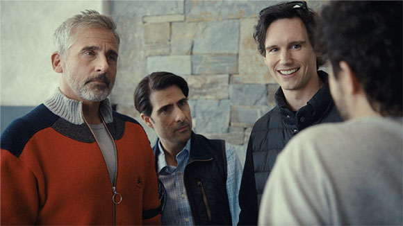 Four men standing in a group indoors against a stone wall.