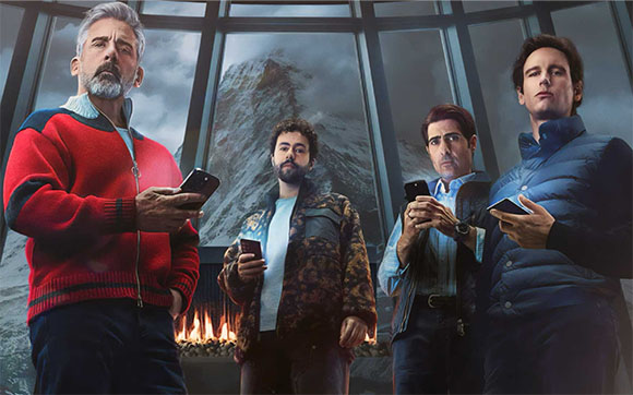 Four men standing indoors, each holding a smartphone, with a mountain landscape visible through a large window.