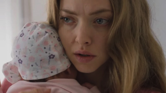 A blonde woman with a concerned expression holds a baby wearing a floral patterned hat.