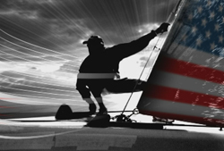 Silhouette of a person leaning out on a sailboat with an American flag patterned sail.