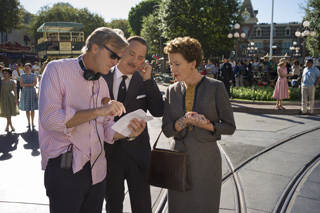 A man in a pink shirt and sunglasses, a man in a suit, and a woman in a grey dress look at a paper together.