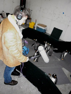 A person wearing headphones and a tan jacket stands near several small penguins in an indoor enclosure.