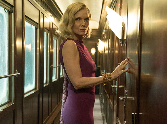 A blonde woman in a purple sleeveless dress stands in a narrow, wood-paneled train hallway.