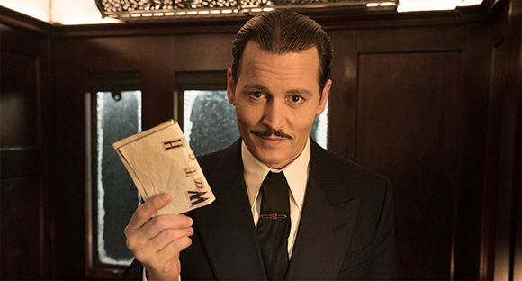 A man with dark hair and a mustache wearing a black suit and tie, holding a small slip of paper.