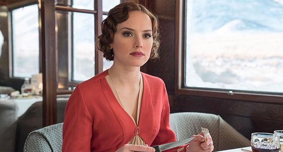 A woman with wavy brown hair wearing a red jacket sits at a dining table near a snowy window view.