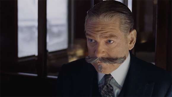 A man with slicked-back hair and a large, grey handlebar mustache wearing a dark suit and tie.