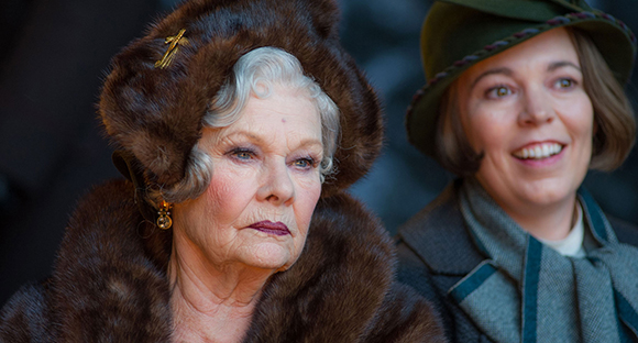 A woman in a brown fur hat and coat looks down while another woman smiles beside her.
