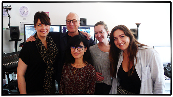 Five people smiling for a group photo in a room with computer monitors and audio equipment.