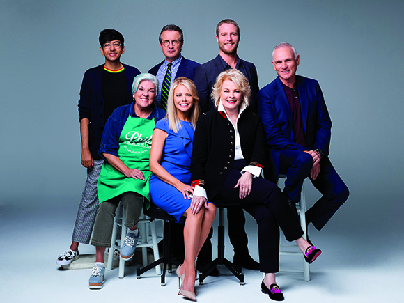 Eight diverse people posing together in a studio against a solid grey background.