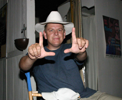 A man wearing a white cowboy hat makes a frame shape with his hands toward the camera.
